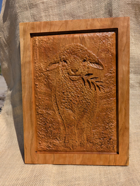 Wooden plaque with a carved sheep design on a textured fabric background