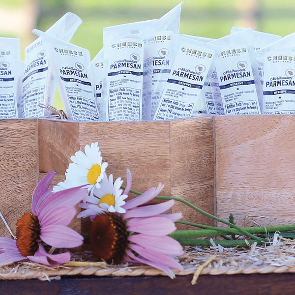 Wooden crate filled with Parmesan cheese packets and flowers on a wooden surface.