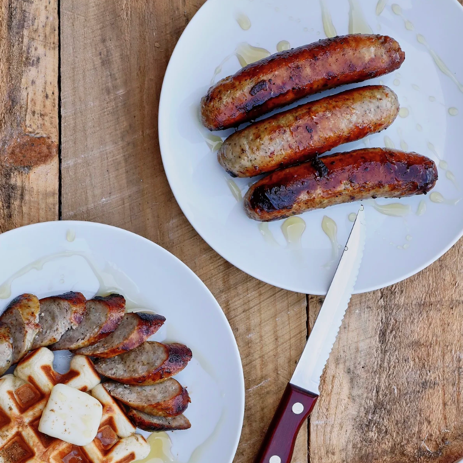 Two plates of sausages on a wooden surface with a knife.