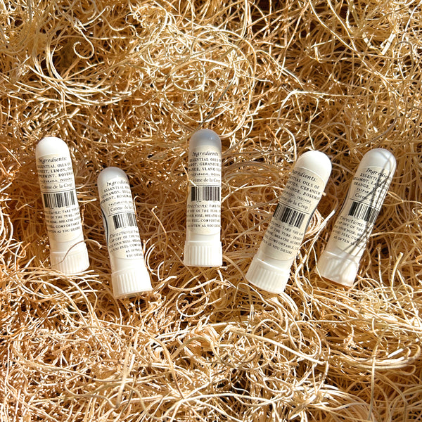 Five small white cylindrical tubes with printed labels and barcode markings, arranged on a bed of loose golden straw or shredded paper.