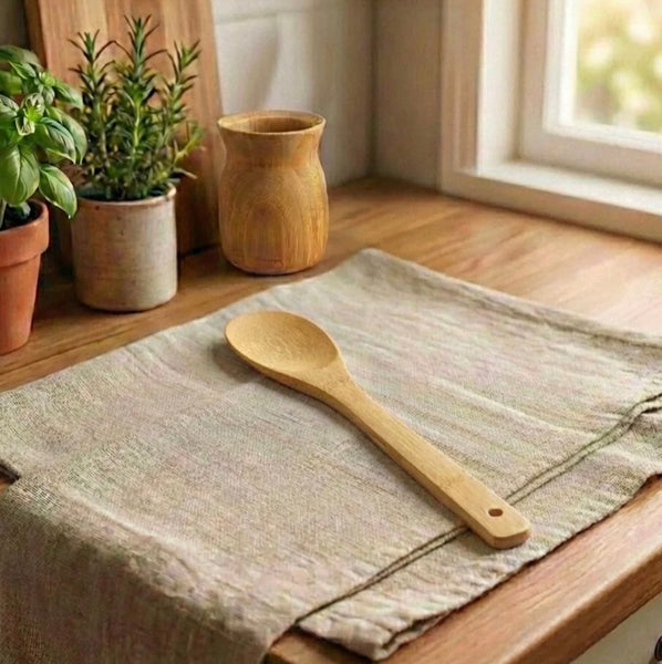 Wooden spoon on a textured cloth with potted plants in the background